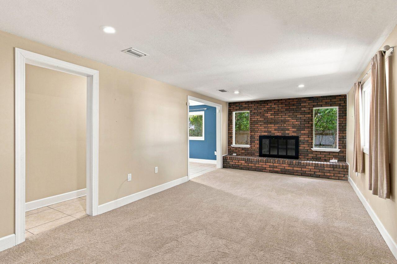 Empty living room with a brick fireplace, beige carpet, and doorway to a blue adjoining room.