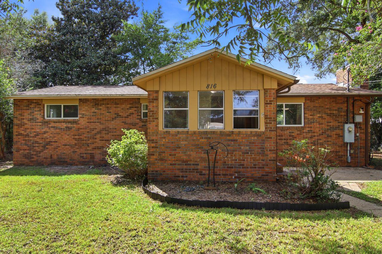 Single-story brick house with tan siding, a projecting front bay, and a shaded lawn.