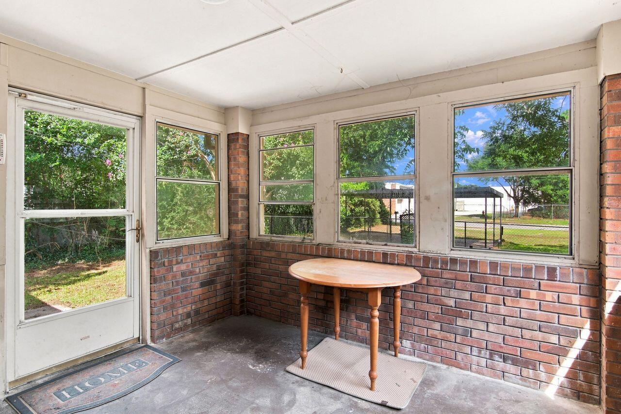 Enclosed porch with brick half-walls, large windows overlooking the yard, and a small wooden table.