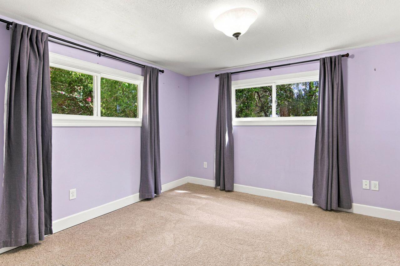 Empty bedroom with purple walls, beige carpet, and two high windows with gray curtains.
