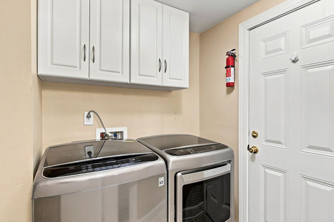 Laundry room with two metallic appliances, white cabinets, and a paneled door.