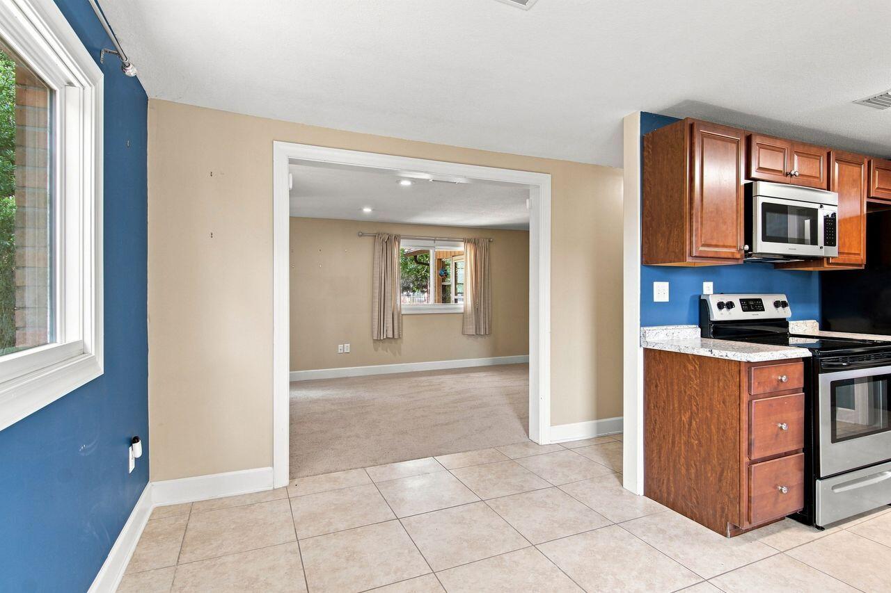 Kitchen with reddish wood cabinets and tiled floor opening onto an empty carpeted room.