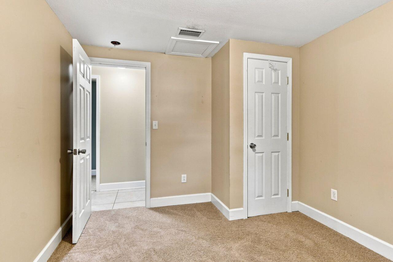 Empty beige room with tan carpet, an open doorway to a tiled hall, and a closed white door.