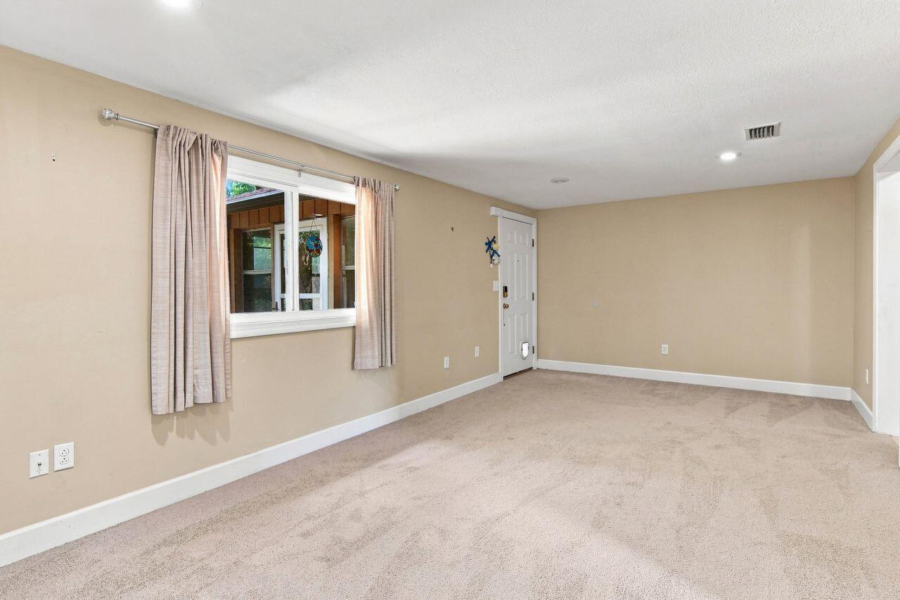 Empty carpeted room with beige walls, a curtained window, and a white door.
