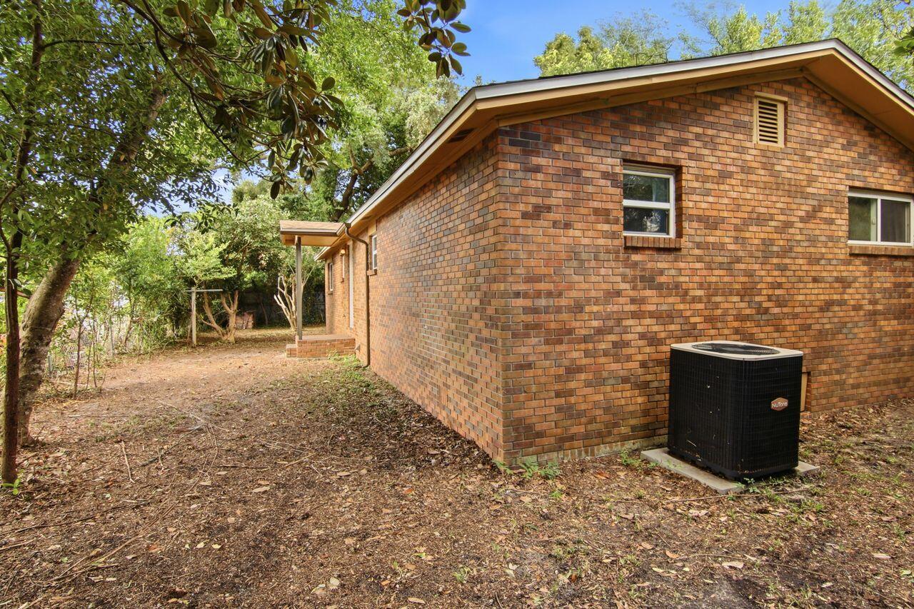 Brick house side with an outdoor air-conditioning unit and covered entrance beneath mature trees.
