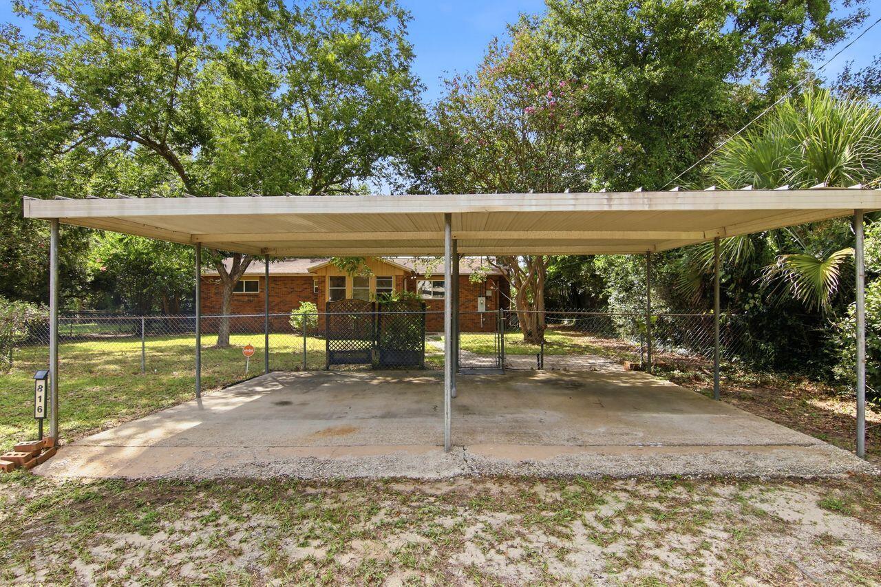 Brick house behind a wide covered carport, with a concrete driveway and fenced yard.