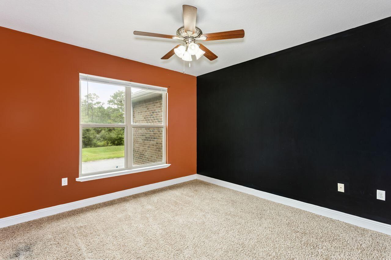 Empty bedroom with rust-orange and black walls, beige carpet, and a window facing a green yard.