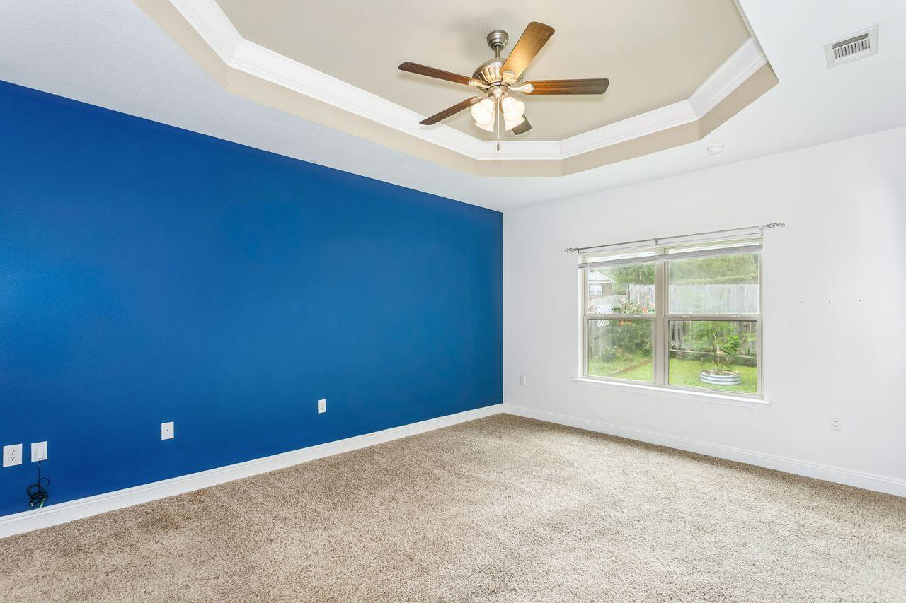 Empty bedroom with a blue accent wall, beige carpet, and tray ceiling with ceiling fan.