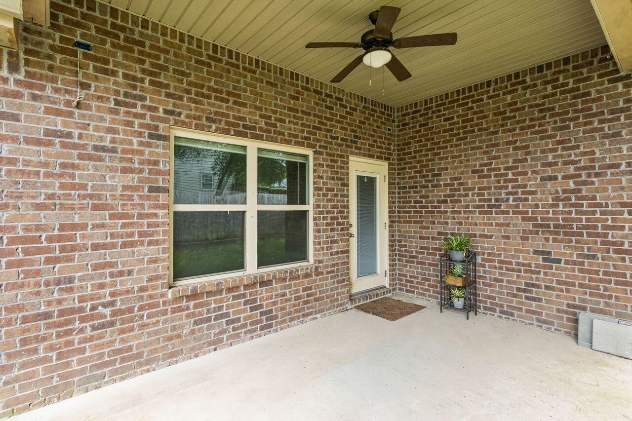 Covered brick patio with a ceiling fan, large window, glass-panel door, and potted plants.