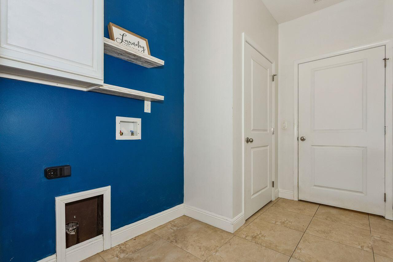 Laundry room with a blue accent wall, white cabinets and shelves, hookups, and beige tile flooring.
