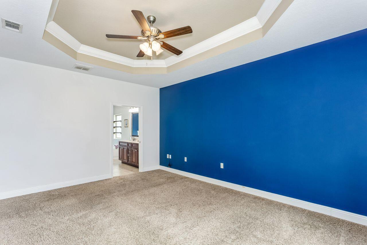 Empty bedroom with a blue accent wall, beige carpet, and tray ceiling fan.