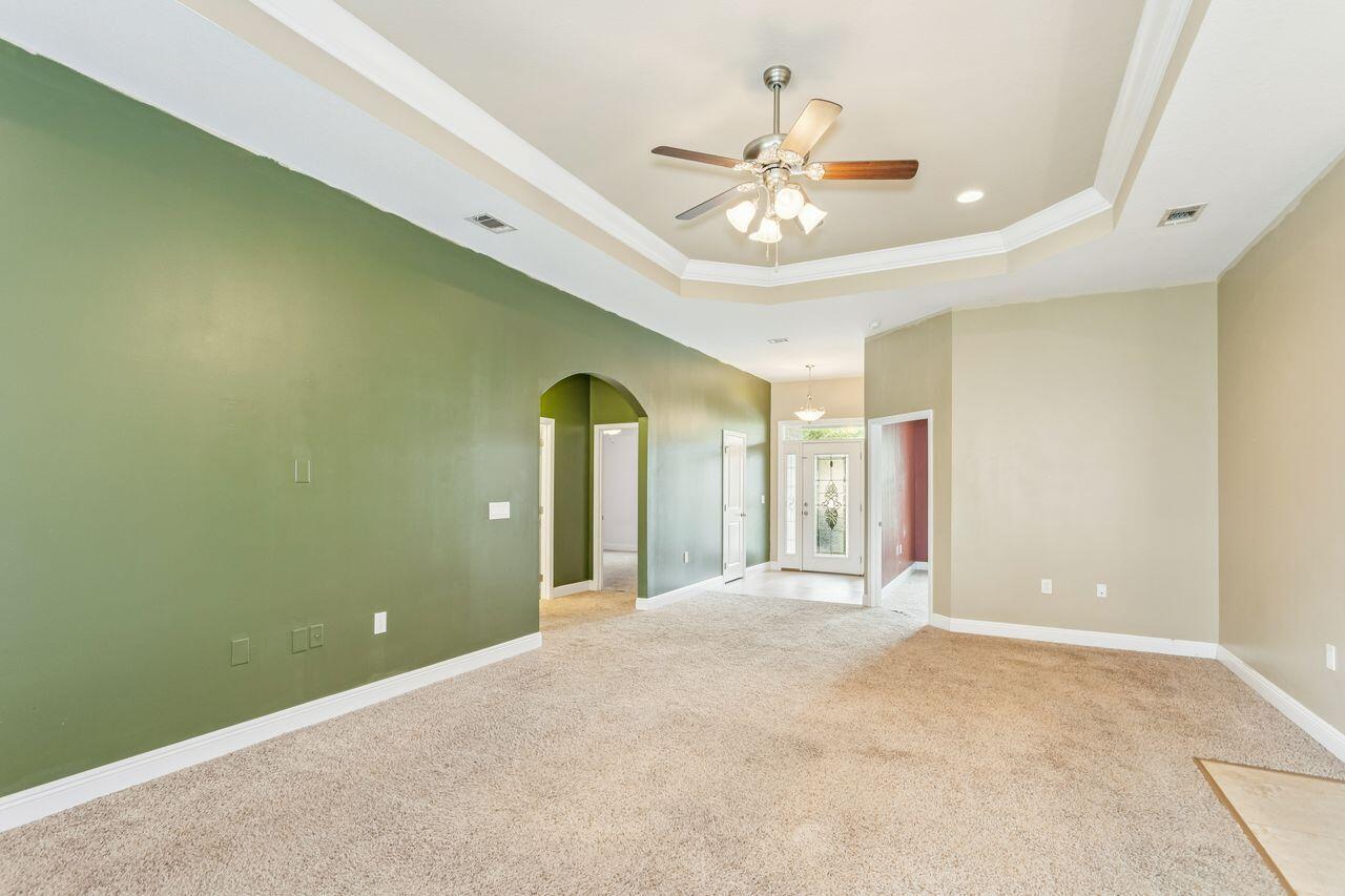 Unfurnished living room with a green accent wall, arched doorway, and tray ceiling with ceiling fan.