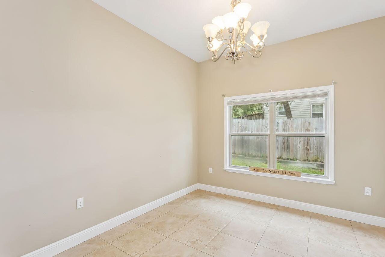 Empty tiled room with a chandelier and a window overlooking a fenced yard.