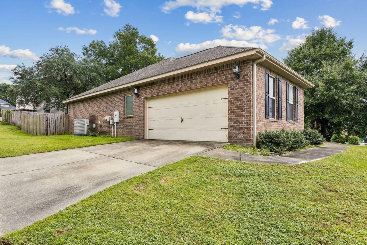 Brick house with a two-car garage, wide concrete driveway, and green lawn.