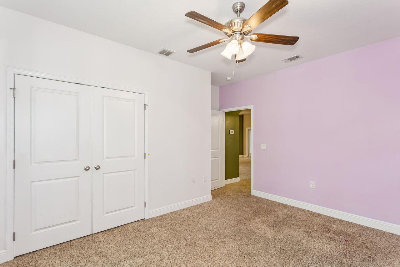 Empty bedroom with beige carpet, white closet doors, a purple wall, and a wooden-blade ceiling fan.