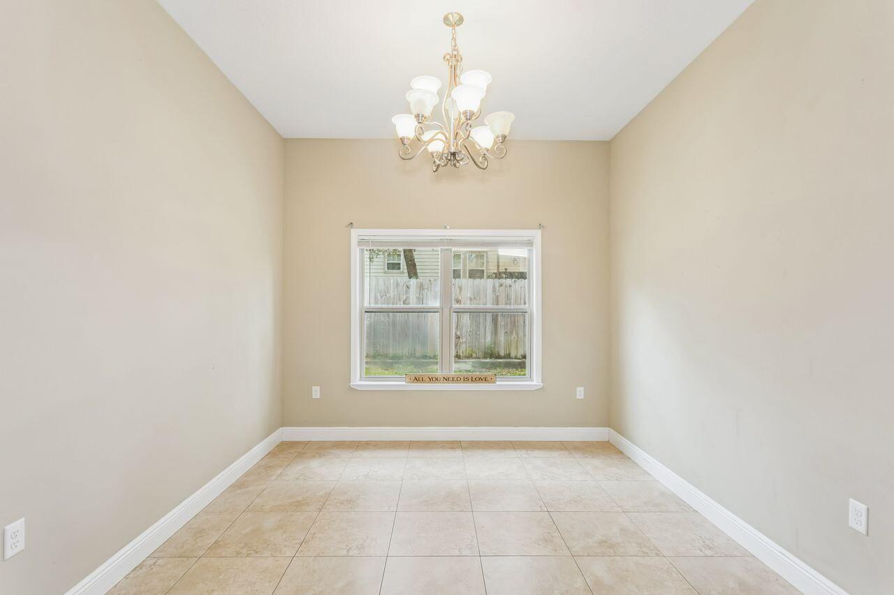 Empty dining room with tan tile flooring, a chandelier, and a window overlooking a fenced yard.