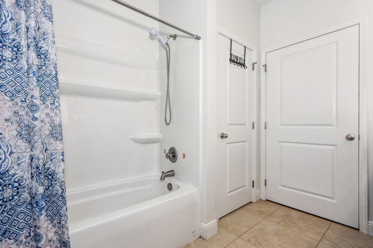 Bathroom tub and shower with a blue patterned curtain and a towel rack labeled “TOWELS”.