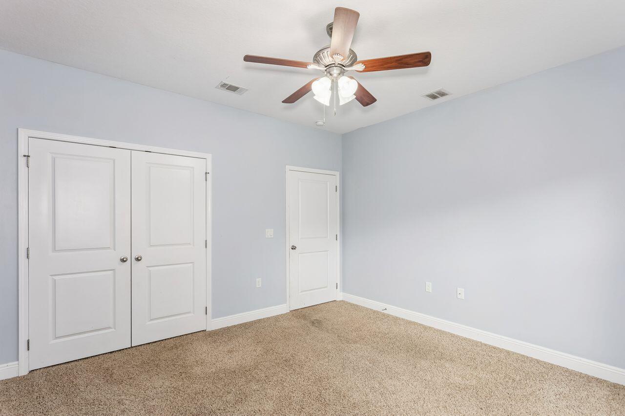 Empty bedroom with beige carpet, white double closet doors, and a ceiling fan.