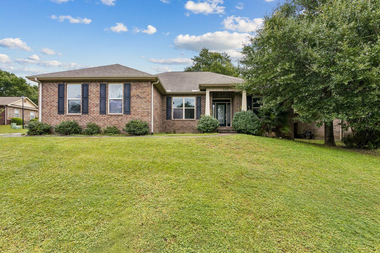 Single-story brick house with dark shutters, covered entry, broad lawn, and mature tree.