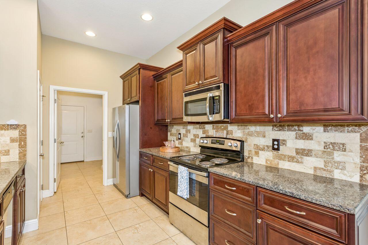 Kitchen with dark wood cabinets, granite counters, patterned tile backsplash, and stainless steel appliances.