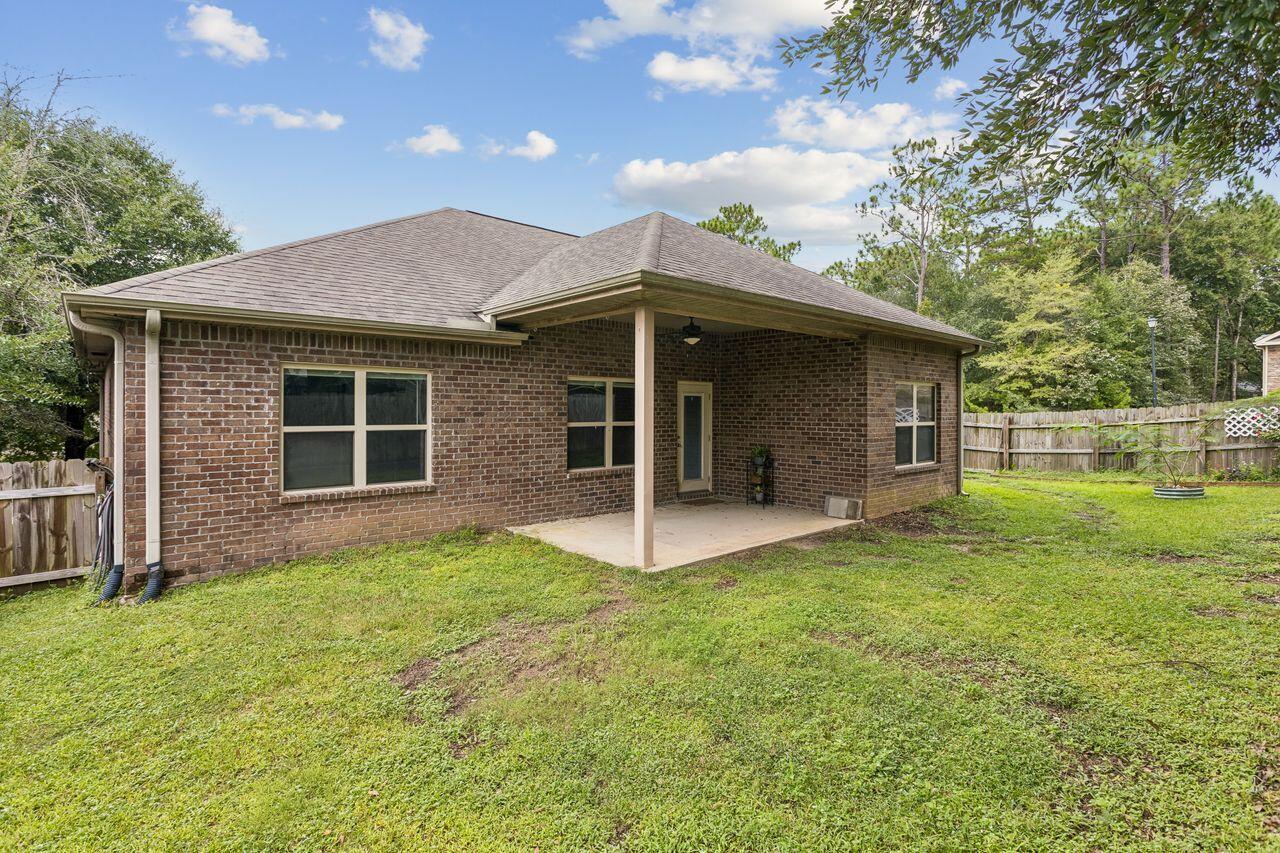 Brick home’s rear exterior with a covered patio and fenced grassy backyard.