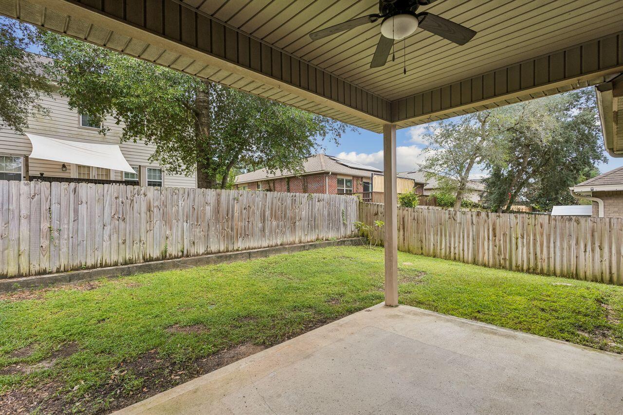 Covered patio with a ceiling fan overlooking a grassy, fenced backyard.