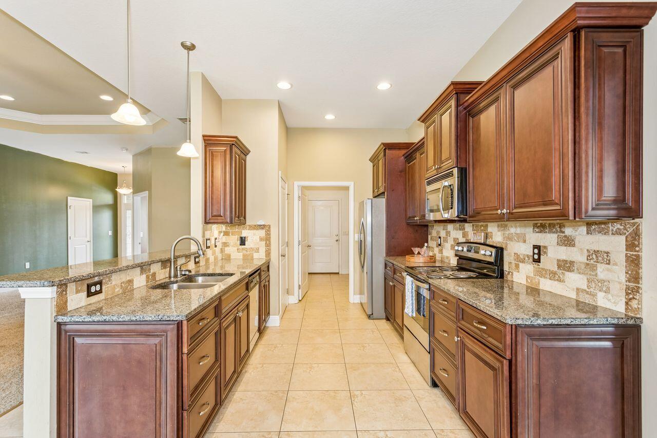 Kitchen with dark wood cabinets, granite counters, stone tile backsplash, and stainless steel appliances.