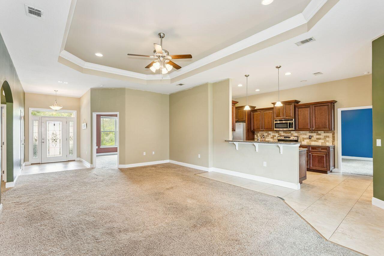 Open living room and kitchen with a tray ceiling, ceiling fan, and dark wood cabinetry.