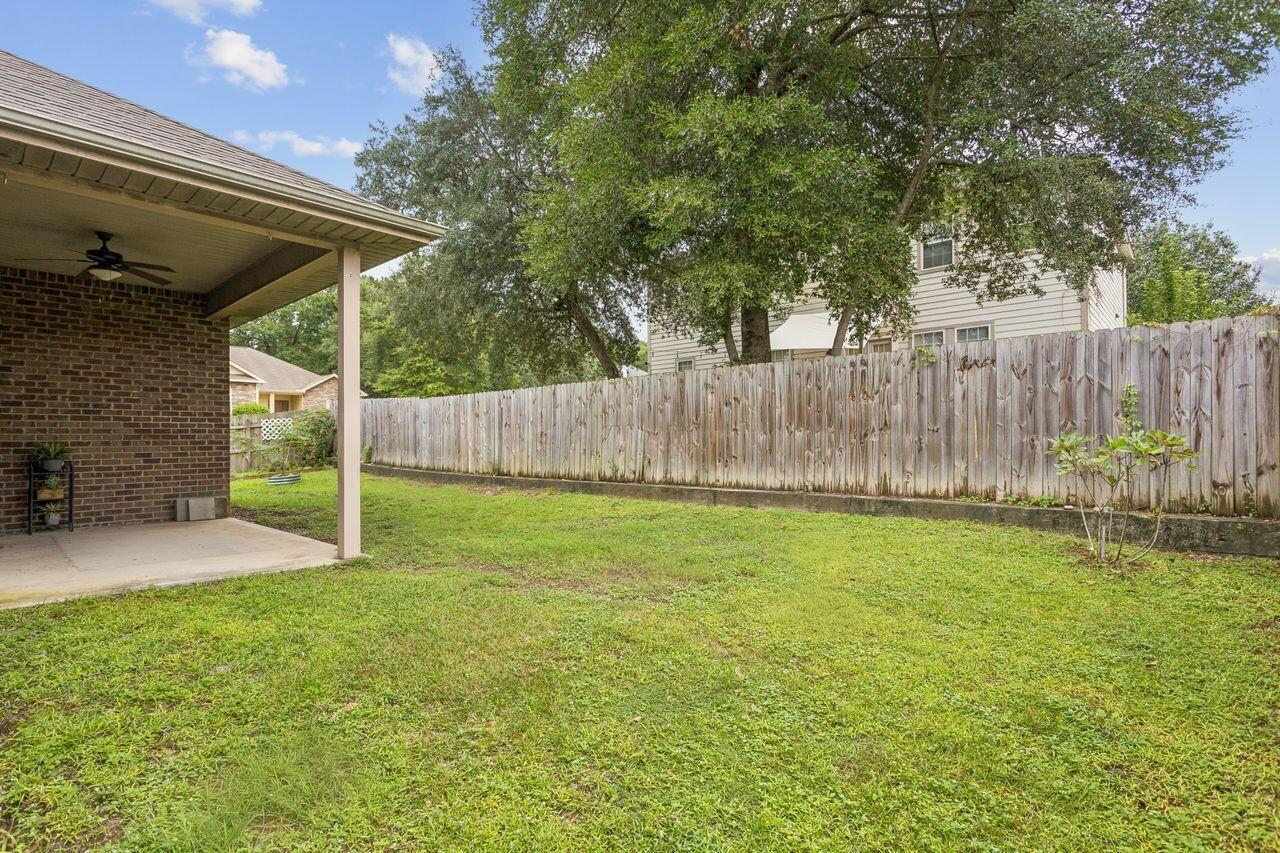 Backyard with a covered brick patio, broad lawn, wooden privacy fence, and mature shade trees.