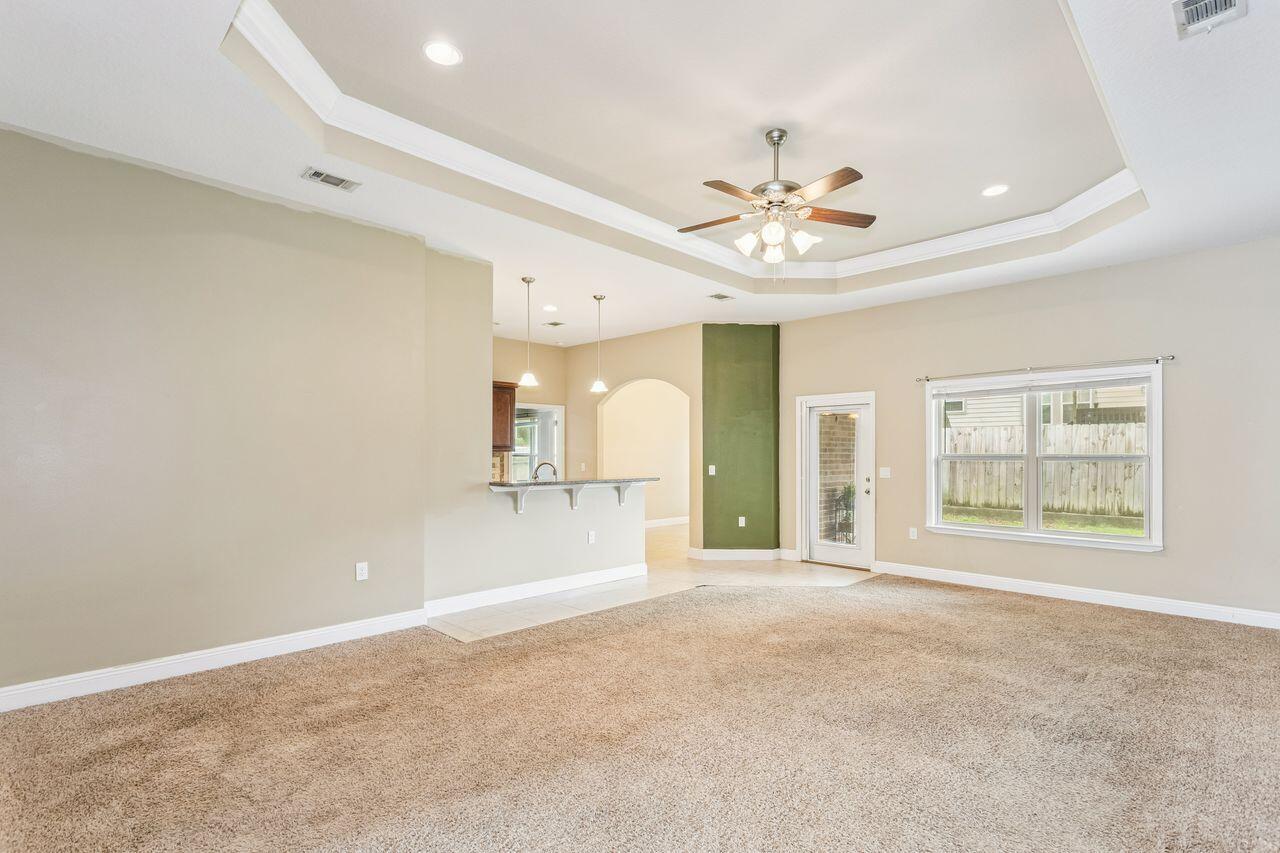 Empty living room with a tray ceiling, ceiling fan, and opening to the kitchen.