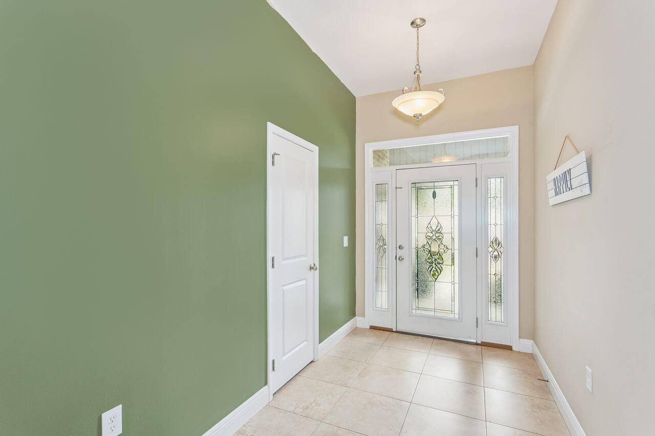 Entry foyer with a decorative glass front door, beige tile floor, and green accent wall.