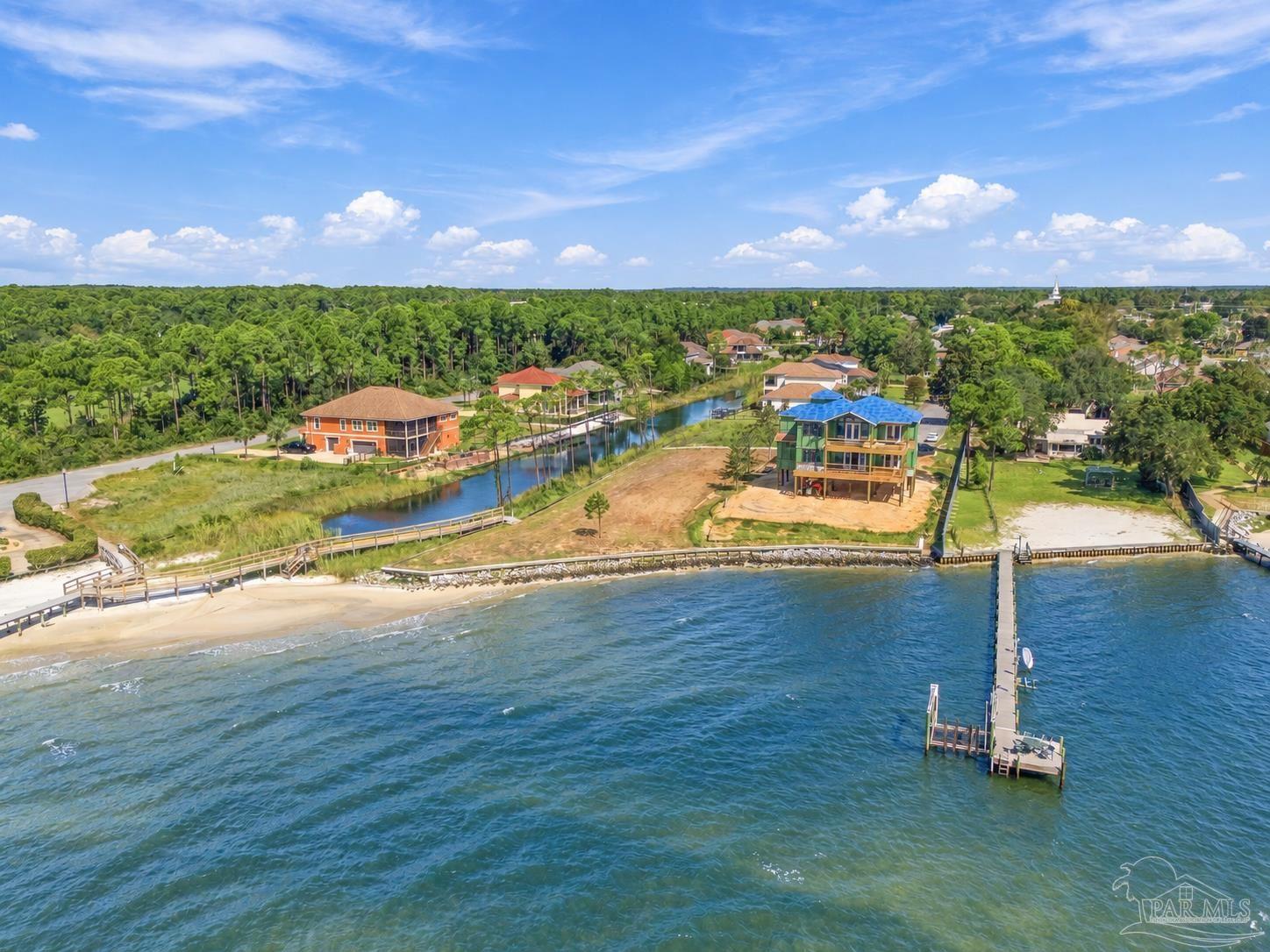 Waterfront home on a sandy lot with a long dock extending into the water.