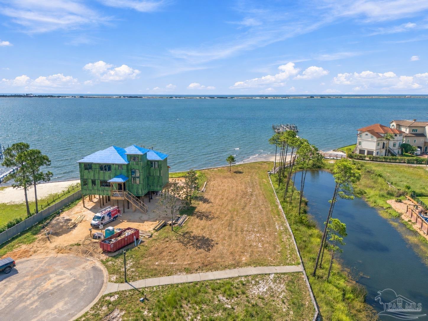 Waterfront lot with a raised house under construction beside a broad bay.