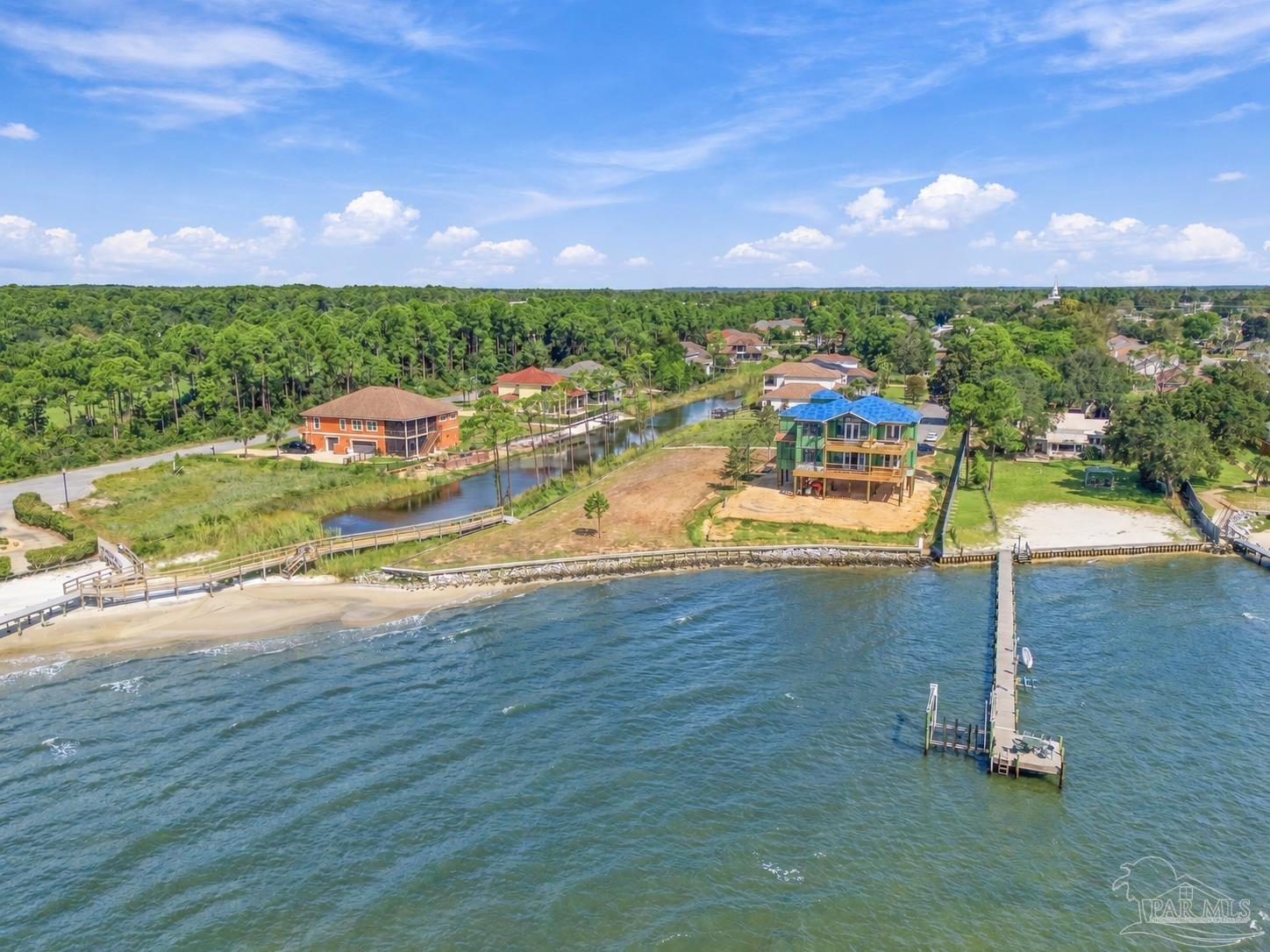 Aerial view of a waterfront home under construction, with a long dock extending into the water.