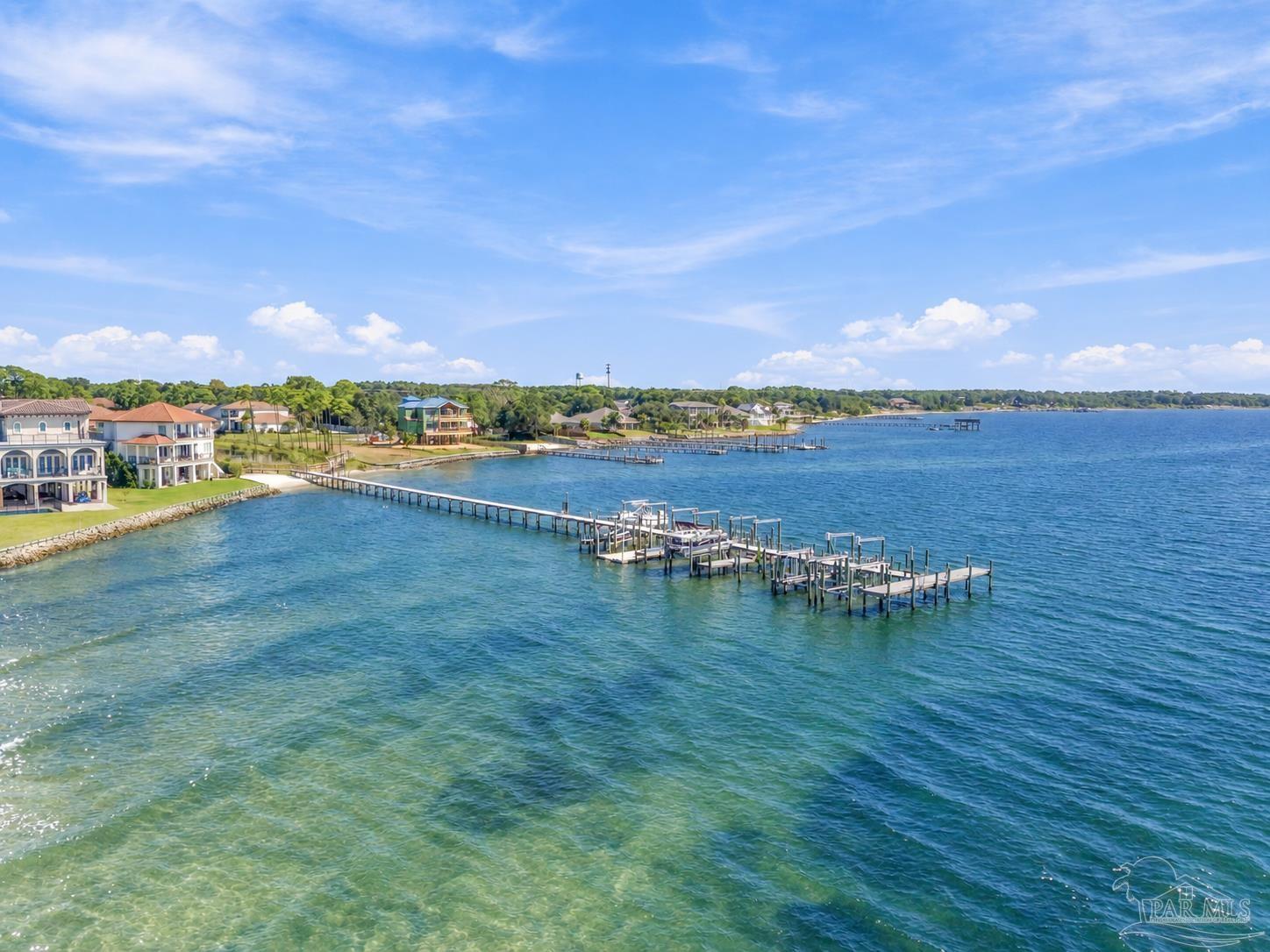 Aerial view of waterfront homes and long docks along a blue bay.