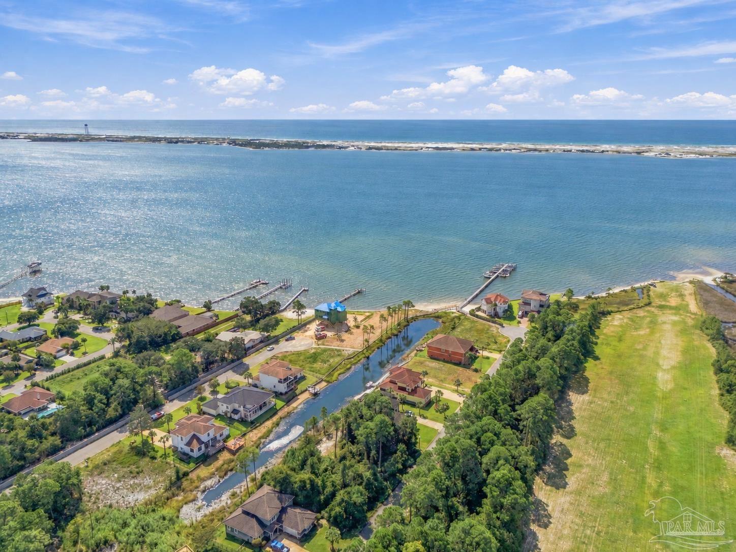 Aerial view of canal-front homes and docks beside a broad bay, with the Gulf beyond.