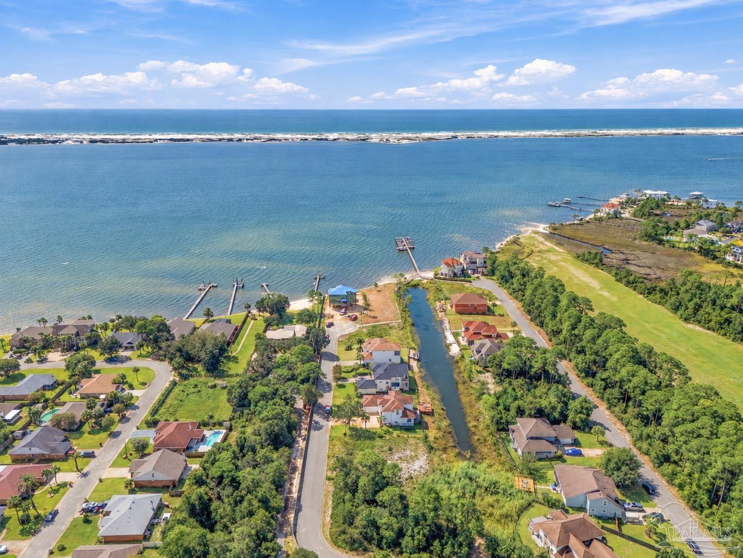 Aerial view of waterfront homes and docks along a bay, with the Gulf beyond a barrier island.