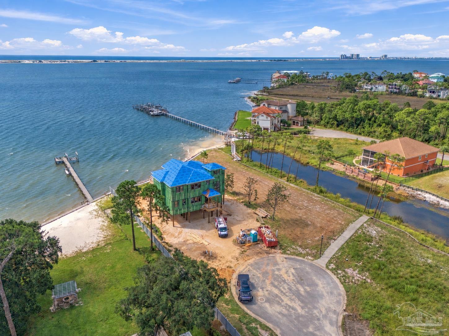 Waterfront home under construction beside a private dock, beach, and neighboring homes.