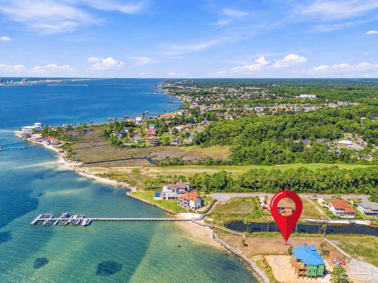 Aerial coastal neighborhood with a red pin marking a waterfront parcel beside homes and docks.