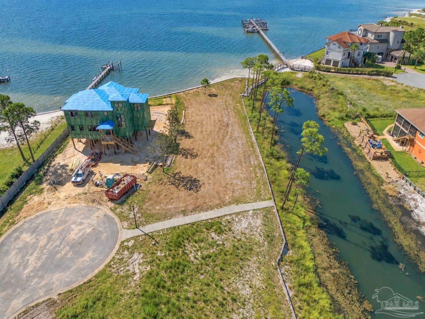 Waterfront construction lot beside a canal and bay, with neighboring homes and docks.