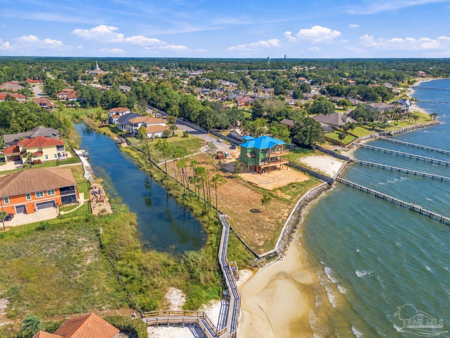 Waterfront home under construction beside a sandy beach, canal, and neighboring docks.