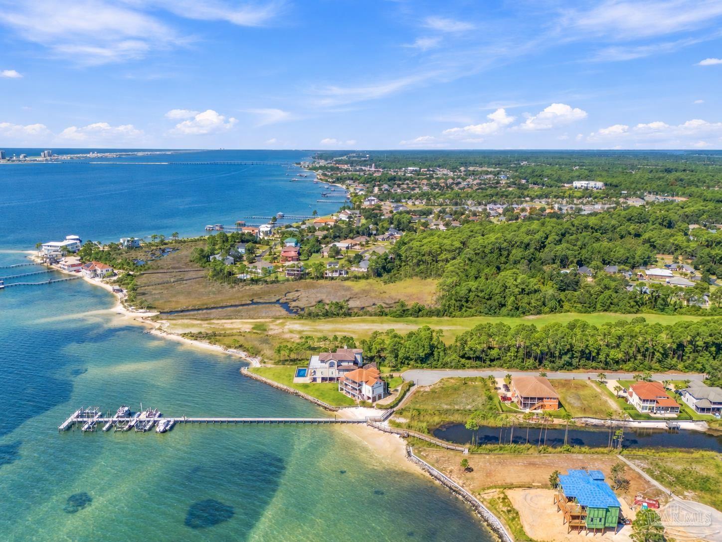 Aerial view of bayfront homes and docks beside a wooded coastal neighborhood.