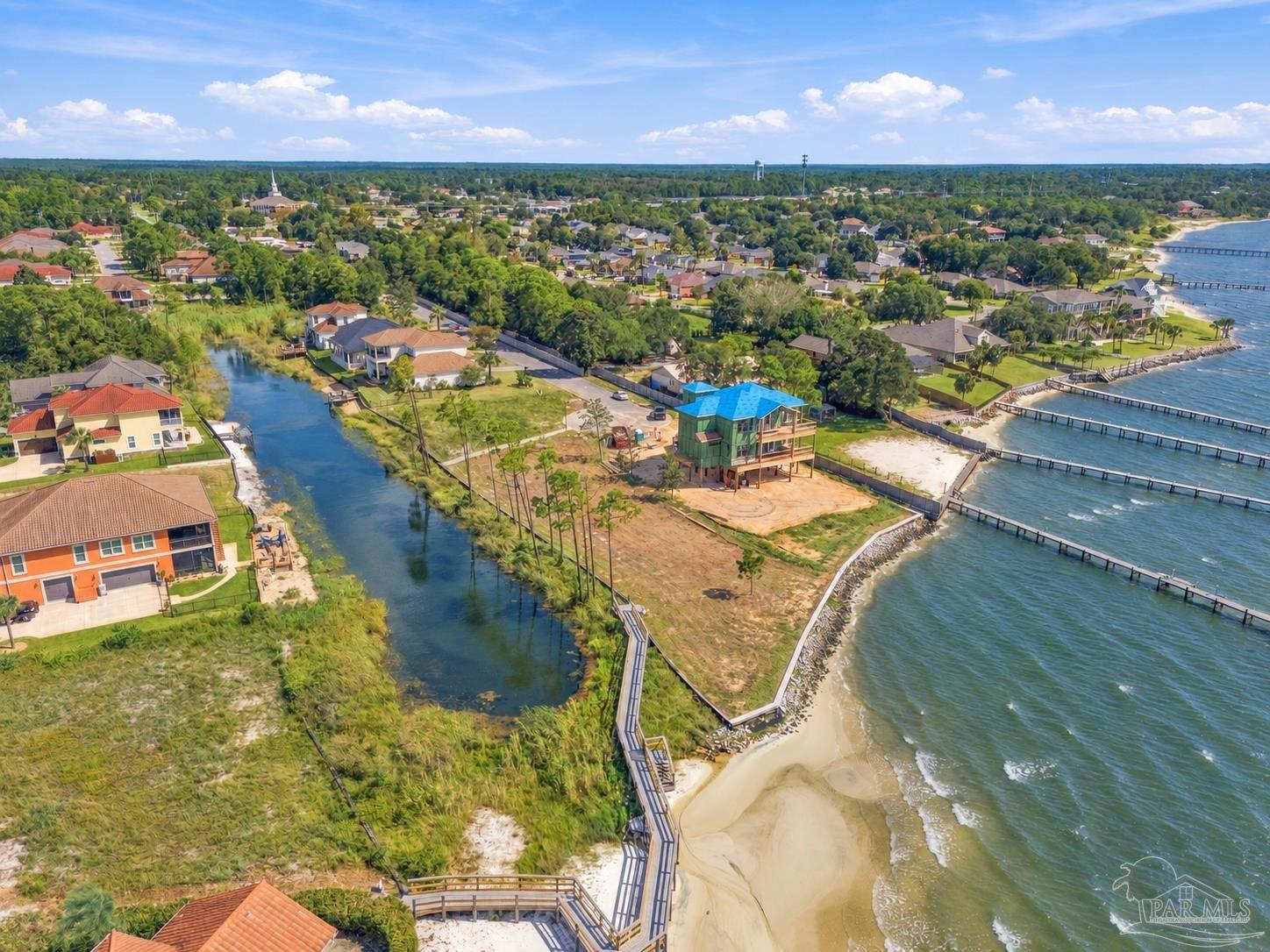Aerial view of a waterfront home under construction beside a canal and sandy shoreline lined with docks.