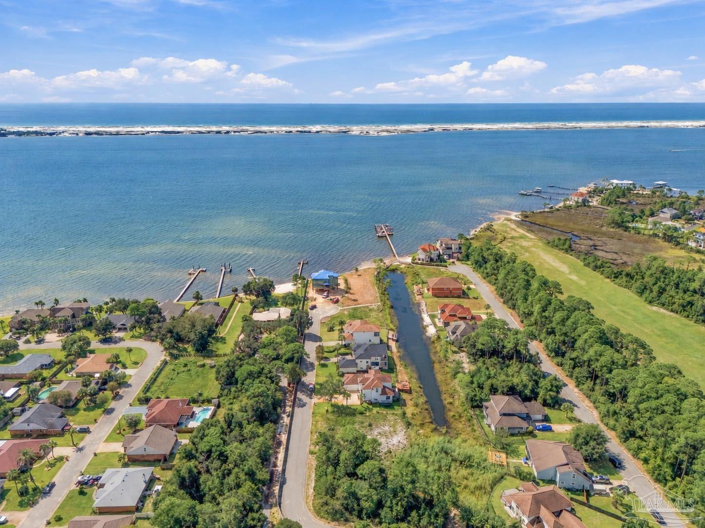 Aerial view of coastal homes and a canal beside a broad bay, with the Gulf shoreline beyond.
