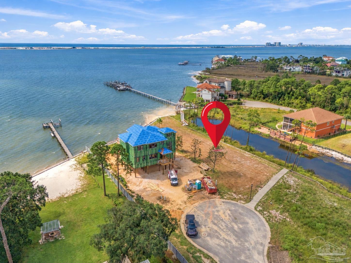 Waterfront construction site marked by a red pin, with a bay, nearby homes, and docks.