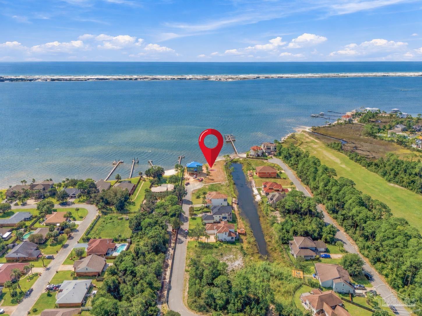 Aerial coastal neighborhood with a red pin marking a waterfront lot beside the bay.