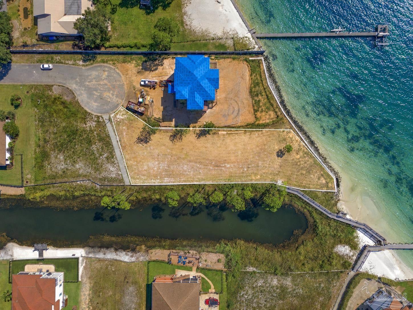 Waterfront home under construction beside a sandy shoreline, with a dock extending into turquoise water.