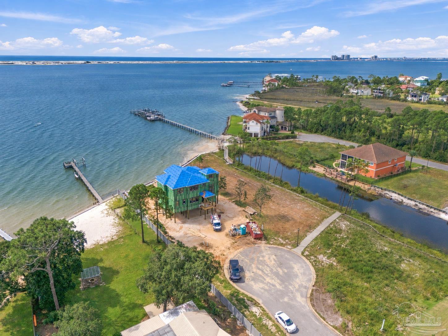 Waterfront home under construction beside a bay, with a blue roof and long private dock.