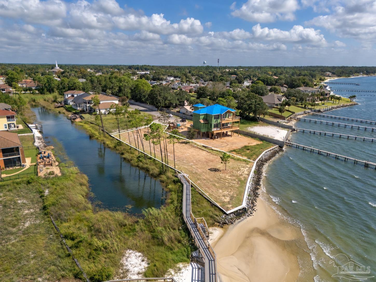 Aerial waterfront property with an elevated home under construction, sandy lot, and long dock.