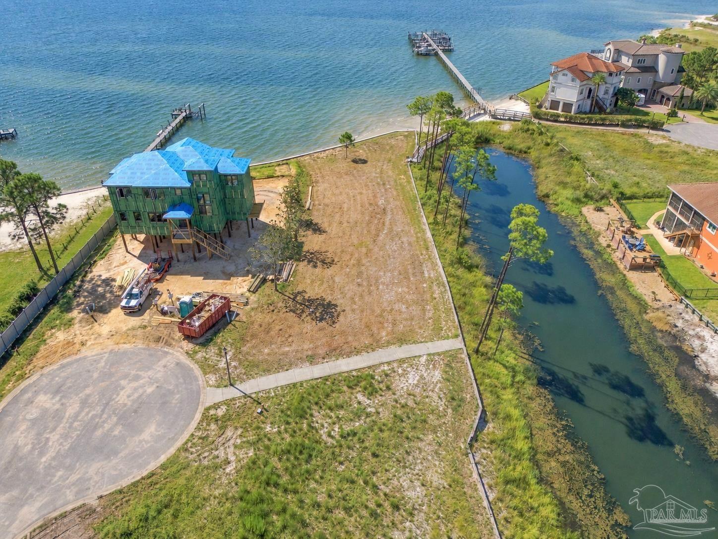 Aerial waterfront lot with a house under construction beside a canal and dock.